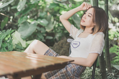 Young woman looking away while sitting against plants