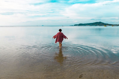 Rear view of man standing on beach against sky