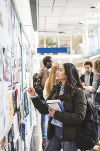 Young female student reading posters in university