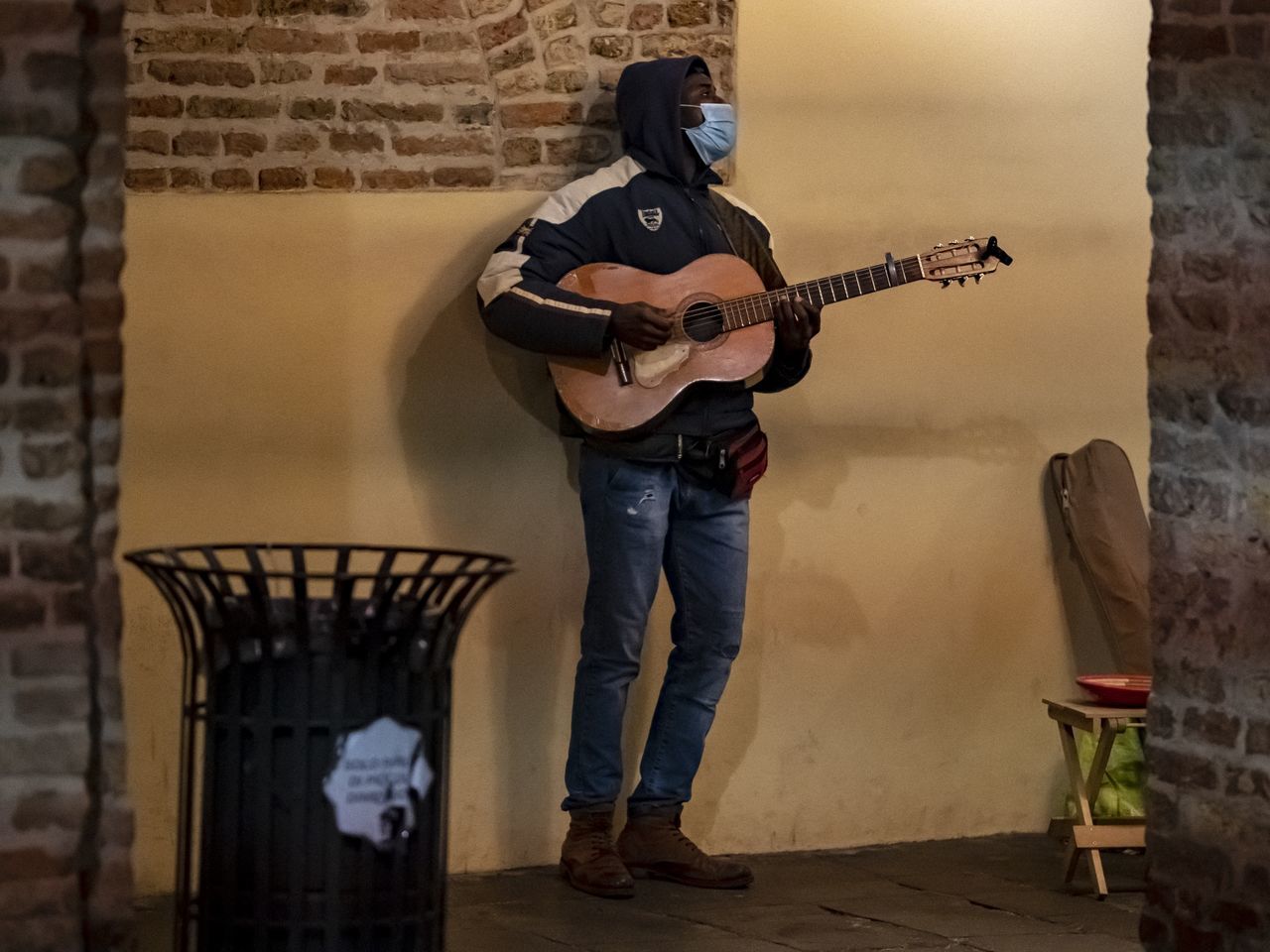 musical instrument, guitar, music, string instrument, musician, brick wall, one person, full length, brick, musical equipment, arts culture and entertainment, adult, wall - building feature, wall, electric guitar, performance, casual clothing, indoors, men, plucking an instrument, standing, skill, young adult, clothing, person, holding, lifestyles