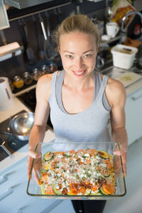 Portrait of smiling woman holding food standing at kitchen