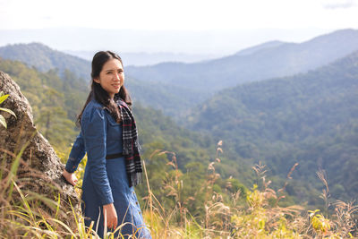 Smiling young woman standing on land against mountains