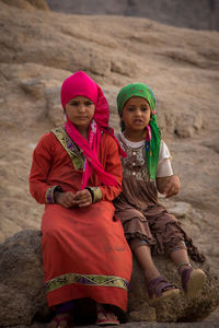Thoughtful sisters wearing headscarves while sitting on rock