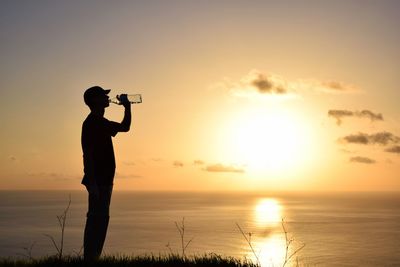 Silhouette man photographing against sky during sunset