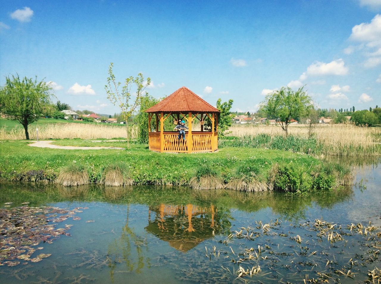 water, built structure, building exterior, sky, architecture, grass, house, tranquil scene, tree, reflection, tranquility, lake, field, nature, rural scene, growth, landscape, scenics, green color, cloud - sky