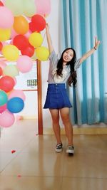 Portrait of young woman gesturing peace sign while standing by balloons in room