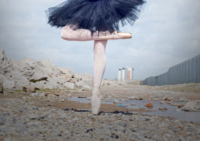 Low section of woman dancing on field against cloudy sky