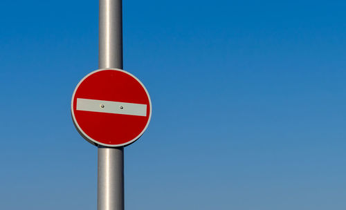 Low angle view of road sign against clear blue sky