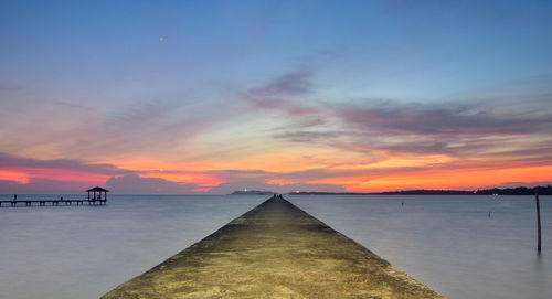 Concrete jetty in sea against sky during sunset