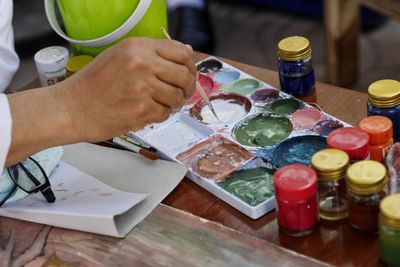 Close-up of person holding paintbrush over palette at table