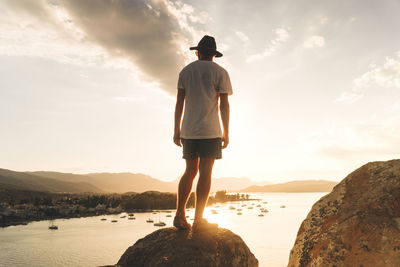 Rear view of man standing on rock against sky