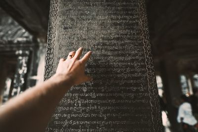 Cropped hand of man reaching towards text on wall at angkor wat temple