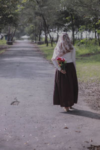 Rear view of woman with flower bouquet walking on footpath