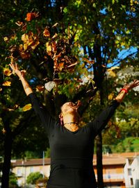 Happy woman throwing autumn leaves at park