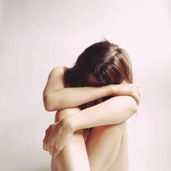 Naked woman sitting against wall at home