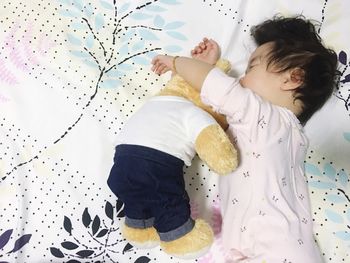 High angle view of cute baby girl lying by teddy bear on bed at home