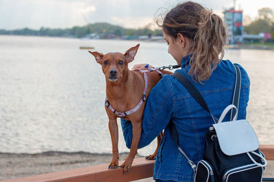 A teen girl holding a miniature pincher in her arms by the of relationship between human and animal.