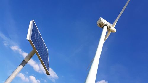 Low angle view of windmill and solar panel against blue sky