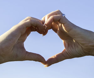 Midsection of man holding heart shape against clear sky