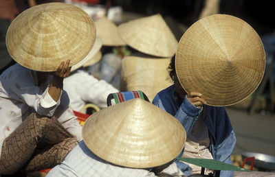 Vendors hiding faces while holding asian style conical hats at market