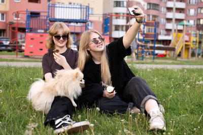 Two funny girls are eating ice cream and playing with a pomeranian dog. taking selfies