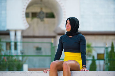 Woman looking away while sitting outside building