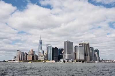 View of city at waterfront against cloudy sky