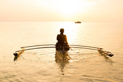 Rear view of man in sea against sky during sunset