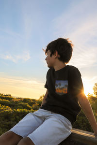 Boy looking at camera against sky during sunset