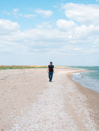 Bearded millennial man in bucket hat walking on empty beach. authentic hipster  outdoor solo travel 