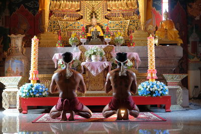 Rear view of shirtless men praying in buddhist temple
