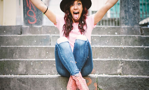 Portrait of excited woman sticking out tongue while sitting on steps