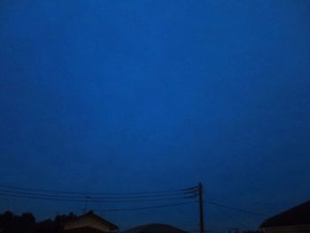 Low angle view of silhouette electricity pylon against blue sky