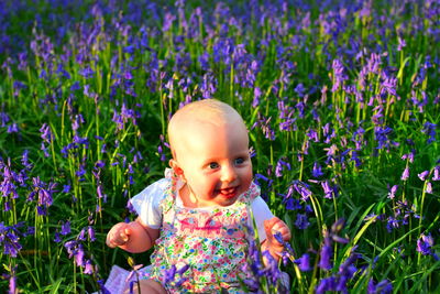 Cute cheerful baby girl sitting amidst flowers on field
