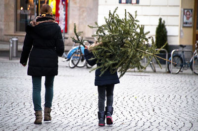 Rear view of woman with son walking on footpath in city during christmas