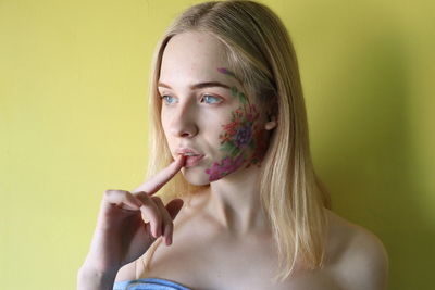 Young woman with painted face against yellow background