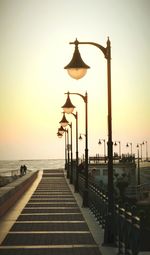 Street light by sea against sky during sunset