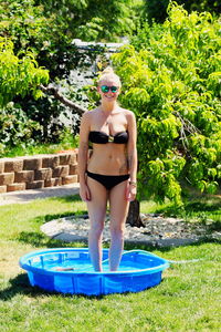 Portrait of smiling beautiful woman in bikini standing on inflatable pool at yard