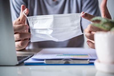 Midsection of man holding white surgical mask at table