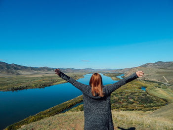 Rear view of woman standing on mountain against blue sky