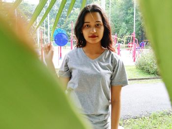 Portrait of beautiful young woman standing against tree