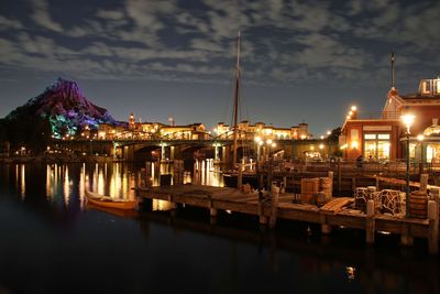 Illuminated buildings by river against sky at night