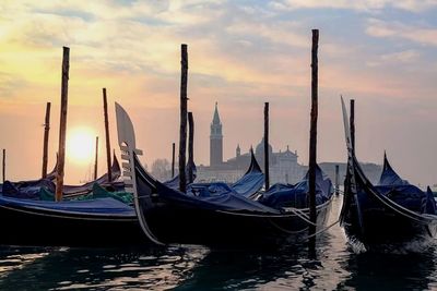 Boats moored in canal against sky during sunset