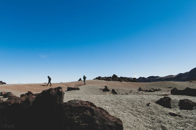 People on desert against clear blue sky