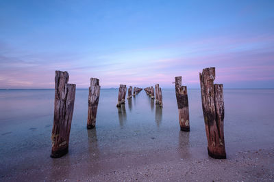 Wooden posts in sea against sky at sunset