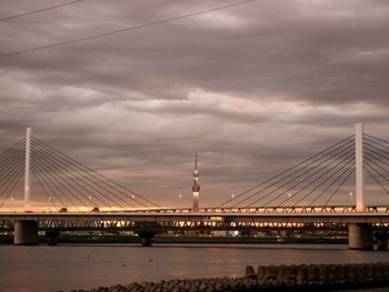 Suspension bridge over river against cloudy sky