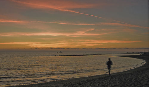 Silhouette man walking on beach against sky during sunset