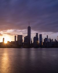 Sea by modern buildings against sky during sunset