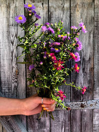 Hand holding flower bouquet against wooden wall