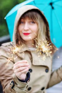 Portrait of smiling woman holding illuminated sparklers outdoors